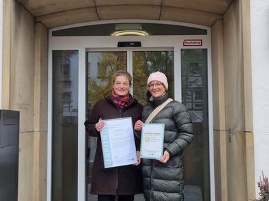 Zwei Personen halten eine Urkunde und eine Plakette