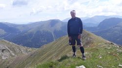 Das Bild zeigt Naturparkführer Holger Kern auf einem Wanderurlaub in den Alpen. Er ist sportlich angezogen und steht erhöht auf einem Berg mit Aussicht in die Bergwelt. 