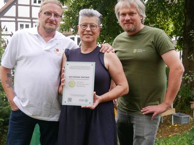 Drei Personen mit einer Urkunde in der Hand