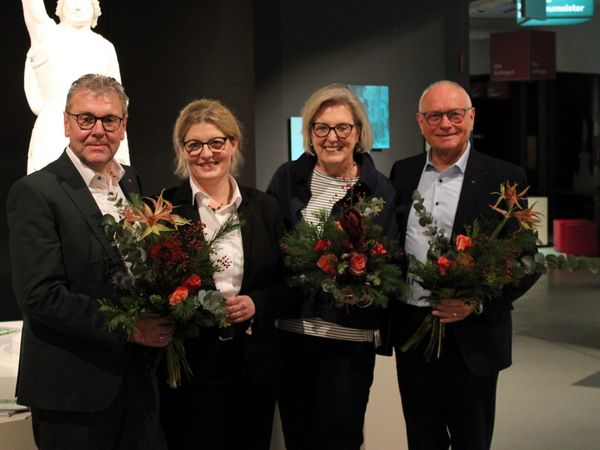 Vier Personen lachen in die Kamera und halten Blumen in der Hand