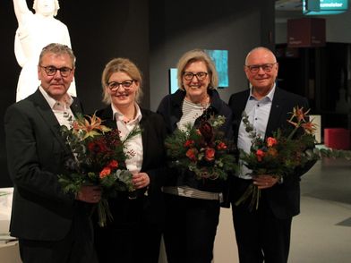 Vier Personen lachen in die Kamera und halten Blumen in der Hand