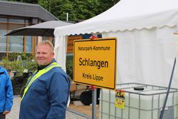 Das Bild zeigt Naturparkführer Henning Schwarze mit blauer Jacke und Warnweste vor dem am Pavillon angebrachten Ortseingangsschild "Naturpark-Kommune Kalletal".