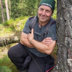 Das Bild zeigt Naturparkführer Kurt Diesterheft hockend an einen Baum gelehnt. Er hat die Arme vor der Brust verschränkt und eine Baumwollmütze auf.