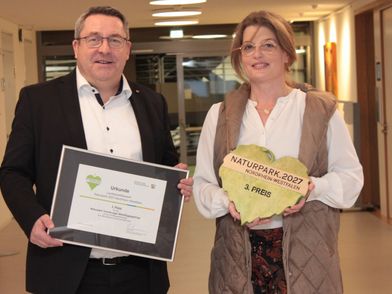 Zwei Personen halten eine Urkunde und eine Plakette in die Kamera