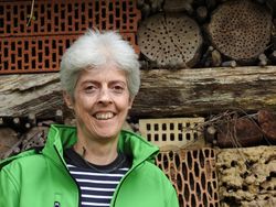 Das Bild zeigt Naturparkführerin Petra Gummert in grüner Jacke. Sie hat graue kurze Haare und steht vor einem großen Insektenhotel.