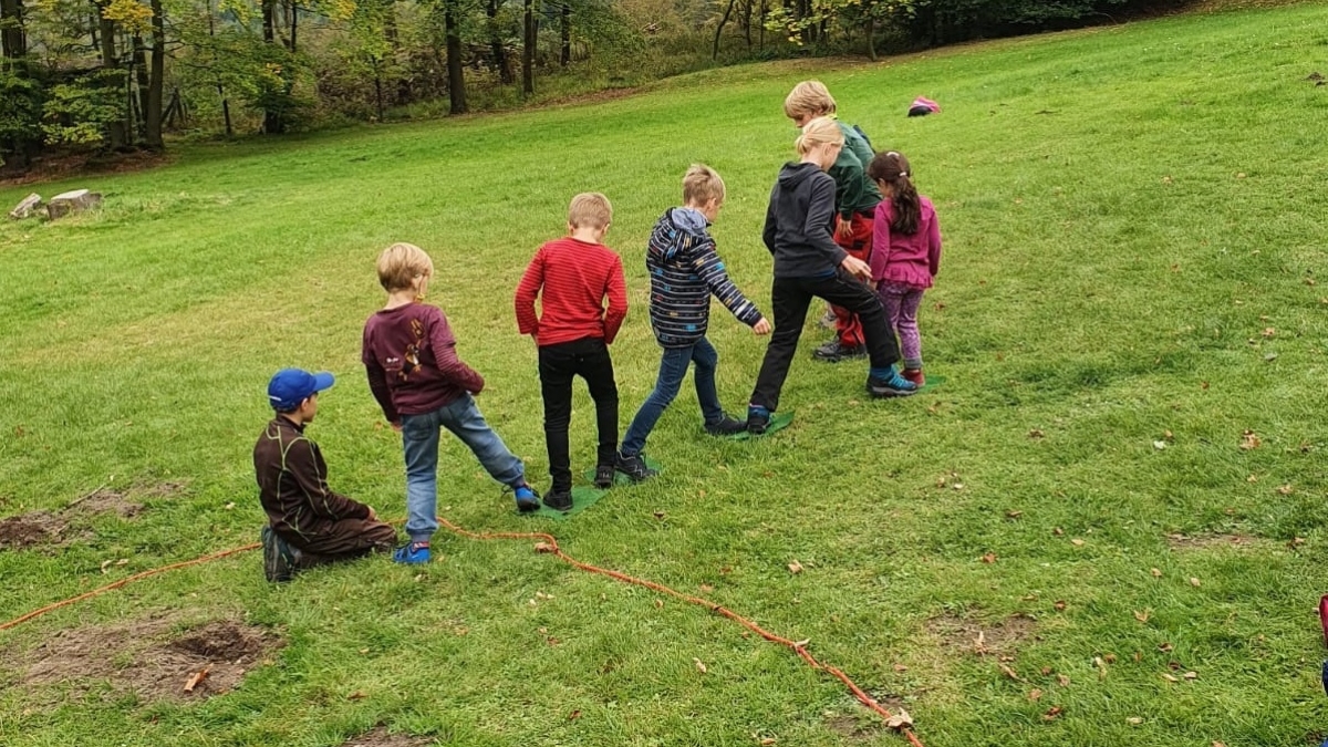 Sieben Kinder spielen nebeneinander auf einer grünen Wiese