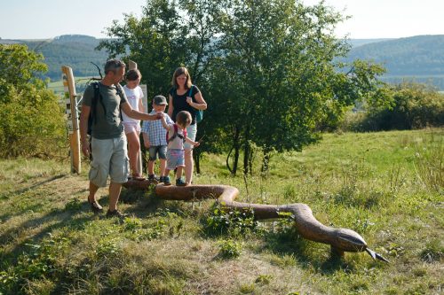 Kinder balancieren auf einer holgeschitzen Schlange, Eltern helfen ihnen